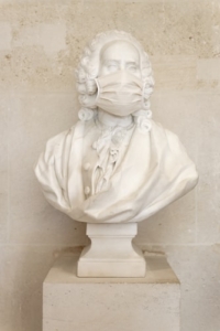 White marble bust of man with curly hair down to shoulders. He is wearing a white surgical mask in reference to the Covid Pandemic.