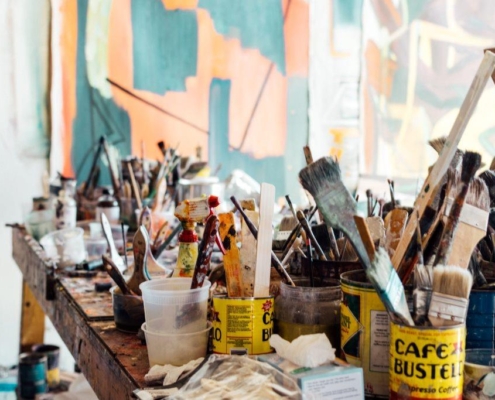 tabletop filled with paintbrushes standing upright in containers