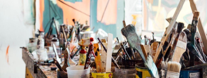 tabletop filled with paintbrushes standing upright in containers