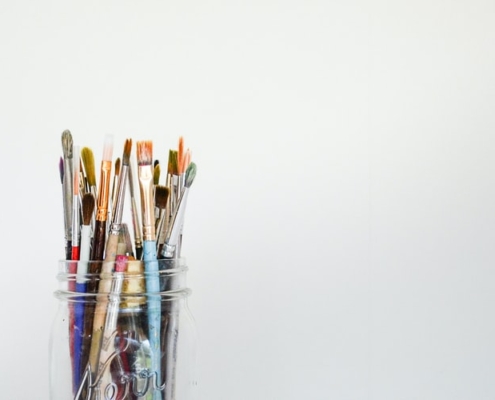 pencil crayons and paint brushes in a clear glass