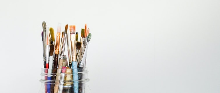 pencil crayons and paint brushes in a clear glass