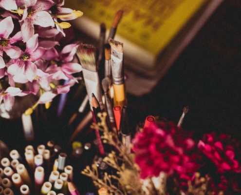 paint brushes in a cup beside a vase of flowers