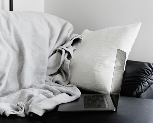 Pillow and blanket on a black couch with a laptop on a coffee table