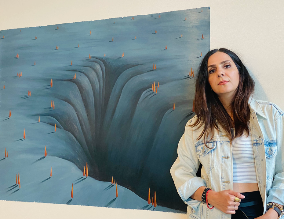 Mohadese posing with her painting that features a blue landscape with red trees throughout