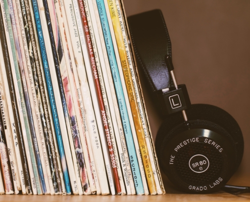 Spines of vinyl records in cardboard cases leaning to the left with black headphones against the records