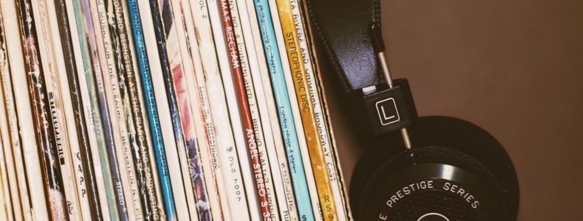 Spines of vinyl records in cardboard cases leaning to the left with black headphones against the records