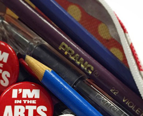 A red pencil case with zipper open and pencil crayons and SAA buttons spilling out