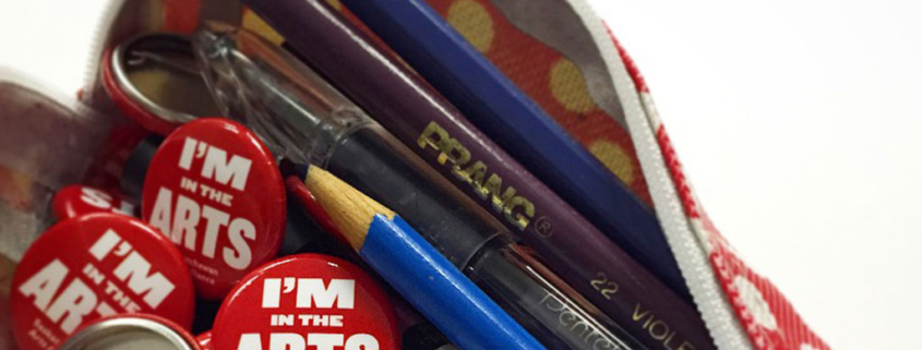 A red pencil case with zipper open and pencil crayons and SAA buttons spilling out