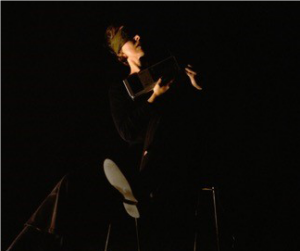 Artist Johanna Bundon in black with black background. Face lit with warm lighting.