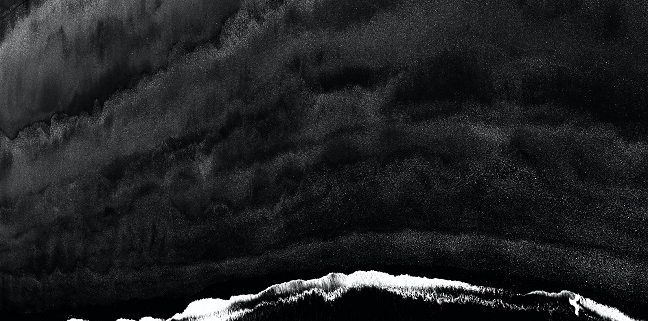 Black and white image of waves hitting the shores - viewpoint from the top.