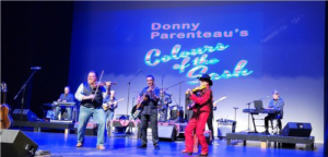 Musician Donny Parenteau plays the fiddle on stage with two other musicians 