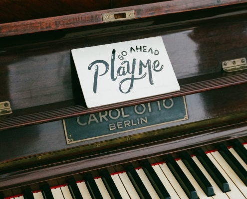 piano with an open keyboard. Above the centre of the piano - above the keys is a hand written note that reads "go ahead, play me."