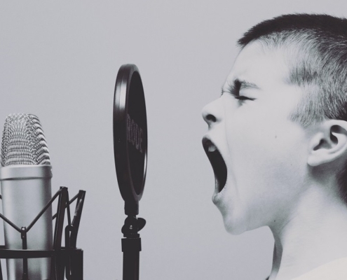 black and white image of boy with brush cut hair singing with mouth wide into a microphone.