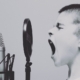 black and white image of boy with brush cut hair singing with mouth wide into a microphone.