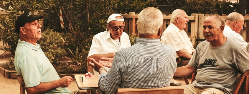 Senior men sitting around an outdoor table in a collective activity.