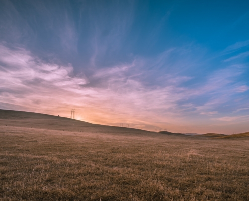 Sunset on the prairies - purpling sky, sun sinking into the horizon of a open prairie landscape. There a power lines in the distance