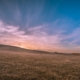 Sunset on the prairies - purpling sky, sun sinking into the horizon of a open prairie landscape. There a power lines in the distance