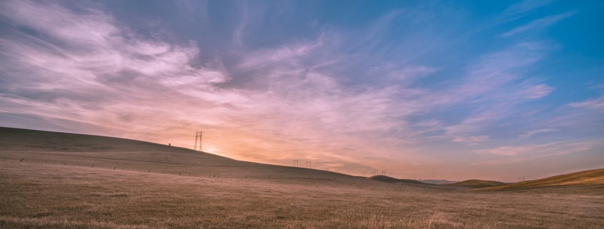 Sunset on the prairies - purpling sky, sun sinking into the horizon of a open prairie landscape. There a power lines in the distance