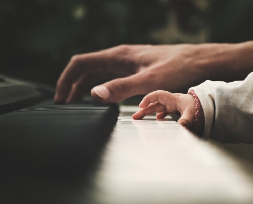 And adult hand plays the piano beside a young toddler hand