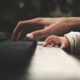 And adult hand plays the piano beside a young toddler hand