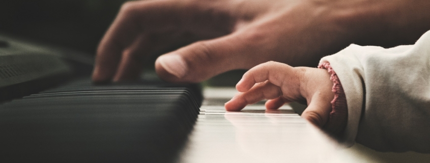 And adult hand plays the piano beside a young toddler hand