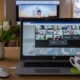 A laptop computer with a view of a Zoom meeting on the screen. There is a structure projected on a screen beyond the computer. There is a white and red polk a dot pitched with with tulips in it to the left of the computer and a white mug with a motivational phrase written on it in black sitting on the laptop.