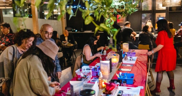 Group of people surrounding a table with arts supplies ready to be used.