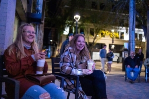 Two women sitting in chairs outdoors in Saskatoon. They are smiling to something off camera. It is night time.