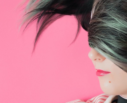 a woman with her hair draped over the top half of her face is earing pig headphones on a pink background