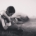 black and white photo of boy with short hair sitting cross legged on the ground playing a guitar.