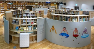 library stacks with colourful books and in the foreground a mural of people painted onto a white half wall.