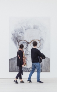 Two people walking in front of large drawing on an older woman.