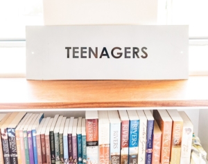 library shelf with young adult books. On the shelf is a label with text of "teenagers."