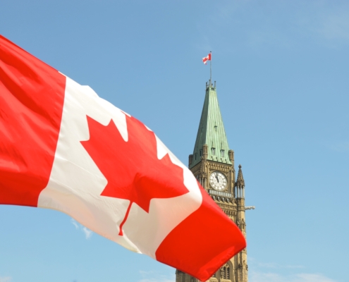 Parliament building in Ottawa with Canadian flag waving in the forefront.