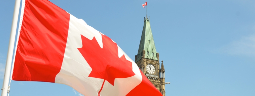 Parliament building in Ottawa with Canadian flag waving in the forefront.