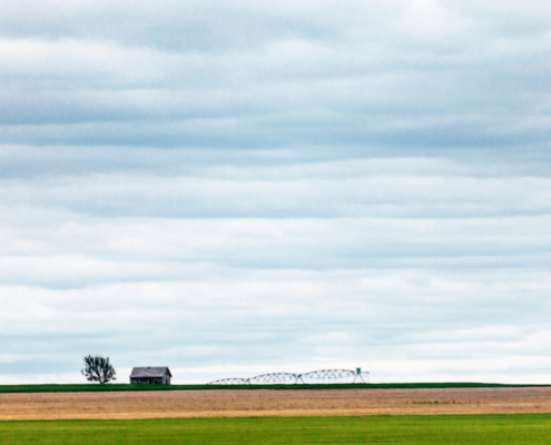 large blue prairie sky with yellow land with a small house in the background.