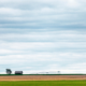 large blue prairie sky with yellow land with a small house in the background.