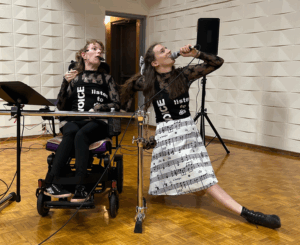 Two performers sing from the SK Arts group Listen to Dis. The one on the right is in an electric wheel chair.
