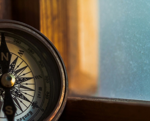 A compass leaning against a windowsill with a blue sky outside