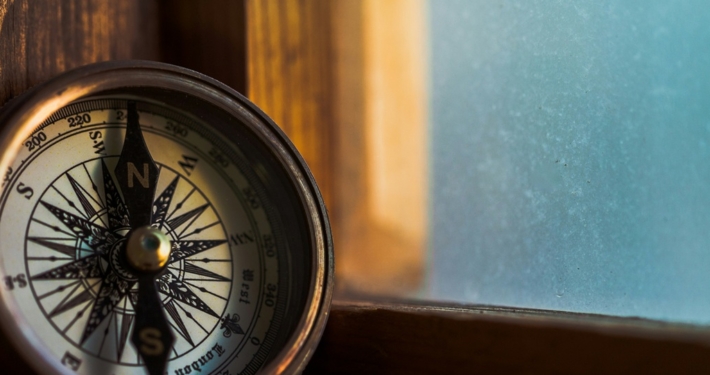 A compass leaning against a windowsill with a blue sky outside