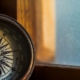 A compass leaning against a windowsill with a blue sky outside