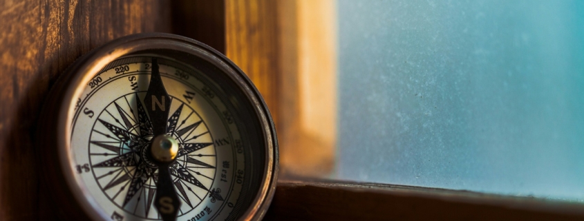 A compass leaning against a windowsill with a blue sky outside