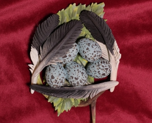 Sculpture by Nikki Little of a bird's nest with blue and brown speckled eggs surrounded by feathers