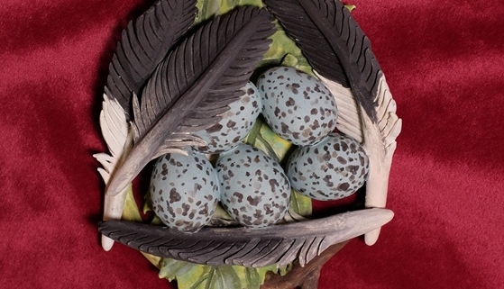 Sculpture by Nikki Little of a bird's nest with blue and brown speckled eggs surrounded by feathers