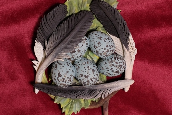 Sculpture by Nikki Little of a bird's nest with blue and brown speckled eggs surrounded by feathers