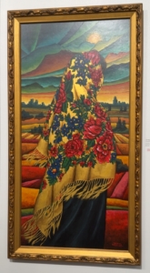 A framed acrylic painting on board by Janaya McCallum depicting a woman wearing a floral kookum scarf, set against a layered landscape backgroun