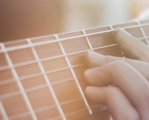 Close-up of the neck of a guitar with a hand placed on a chord. Sun shining down on both
