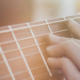Close-up of the neck of a guitar with a hand placed on a chord. Sun shining down on both