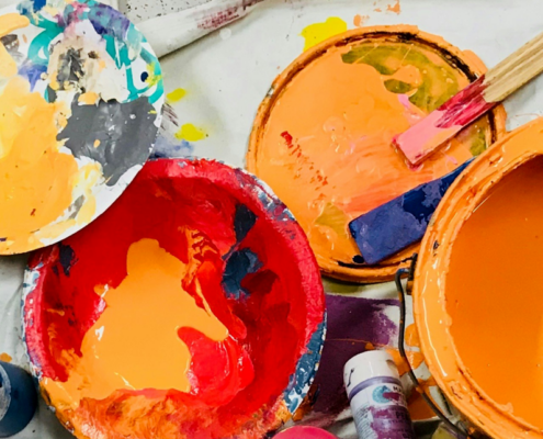 bowls and buckets of paint from orange, purple, pink and yellow on a drop cloth