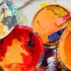 bowls and buckets of paint from orange, purple, pink and yellow on a drop cloth